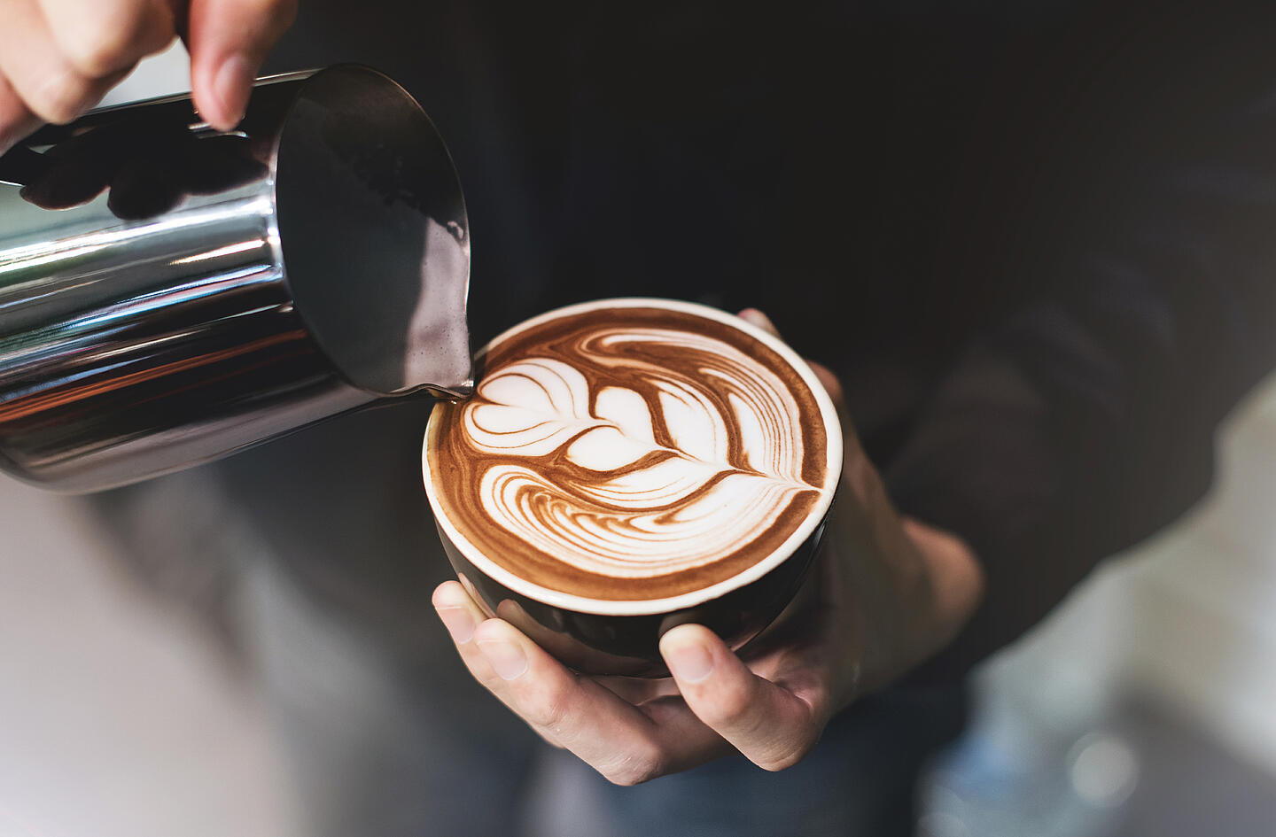 Barista gießt Latte Art in einen Cappuccino